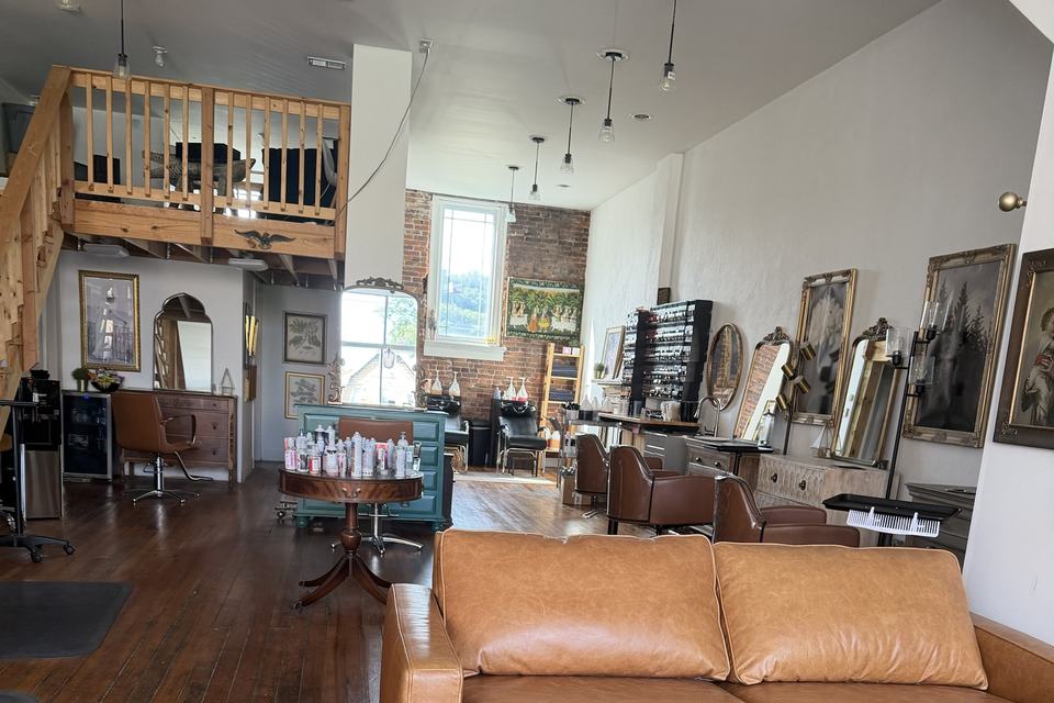 Inside the Canonsburg studio: color stations and mirrors on dark plank floors, beneath a timber loft and an exposed brick wall.
